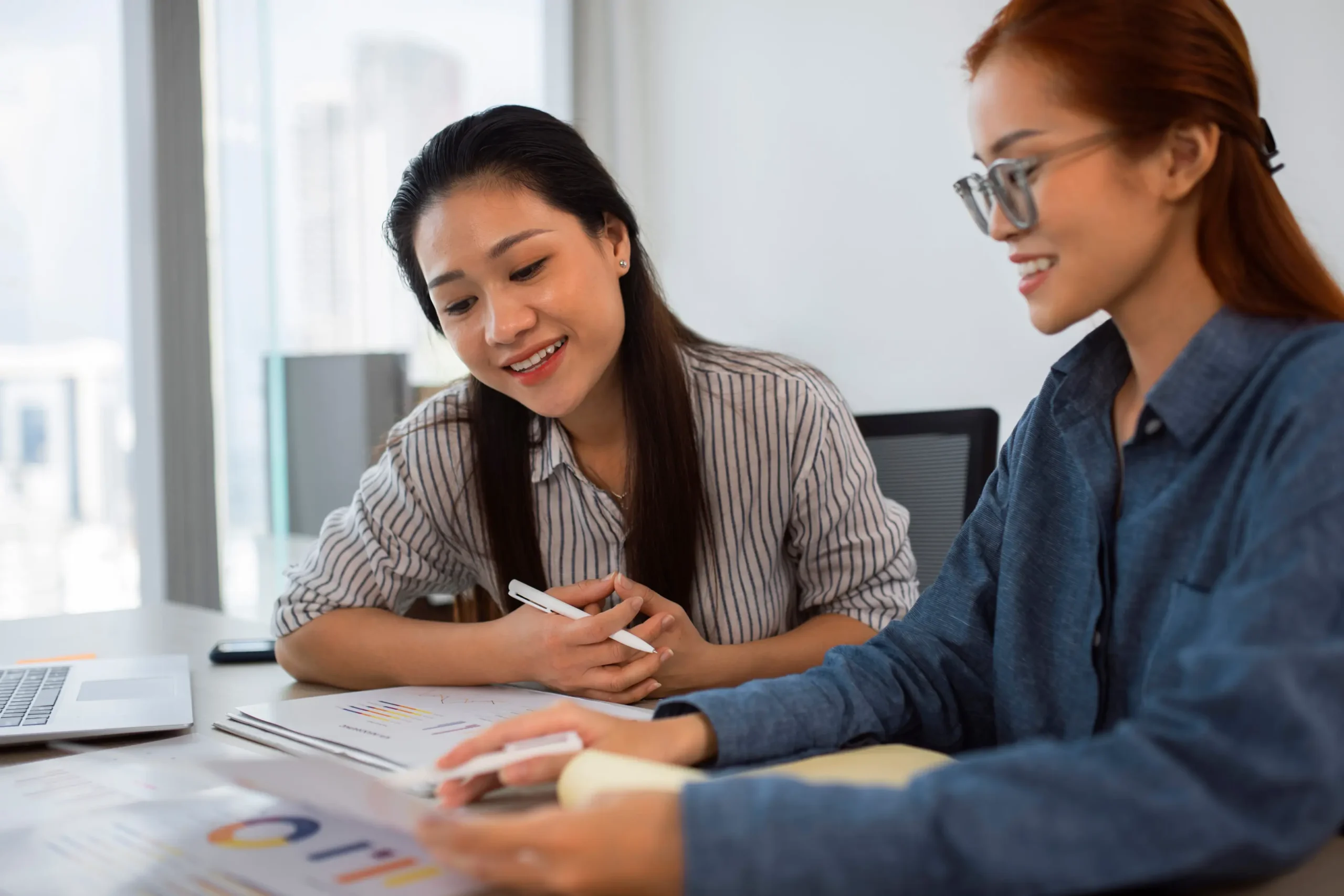 Two colleagues reviewing printed charts and discussing investment performance at a bright office desk.