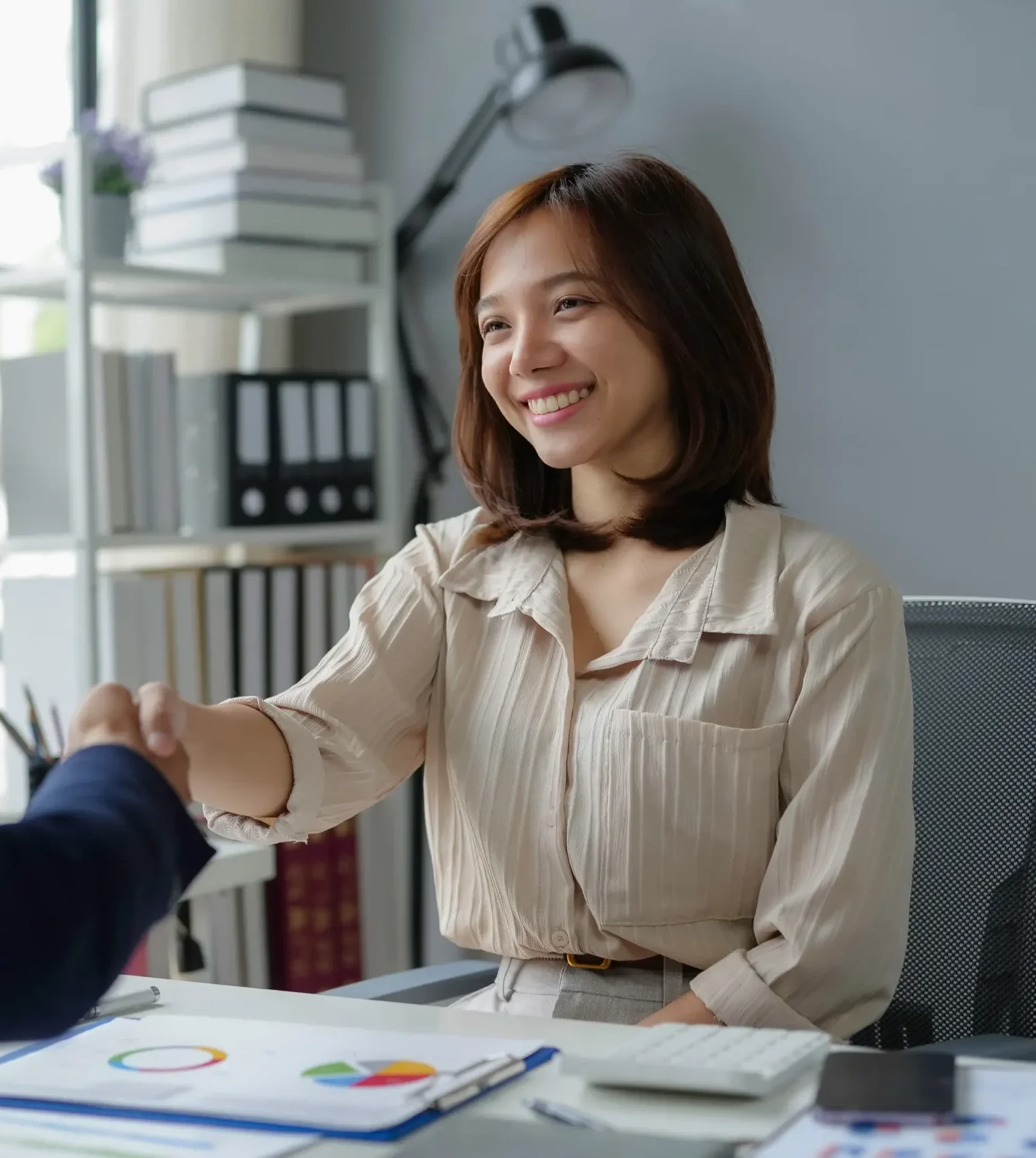Smiling investment adviser shaking hands with client across desk after discussing portfolio performance.