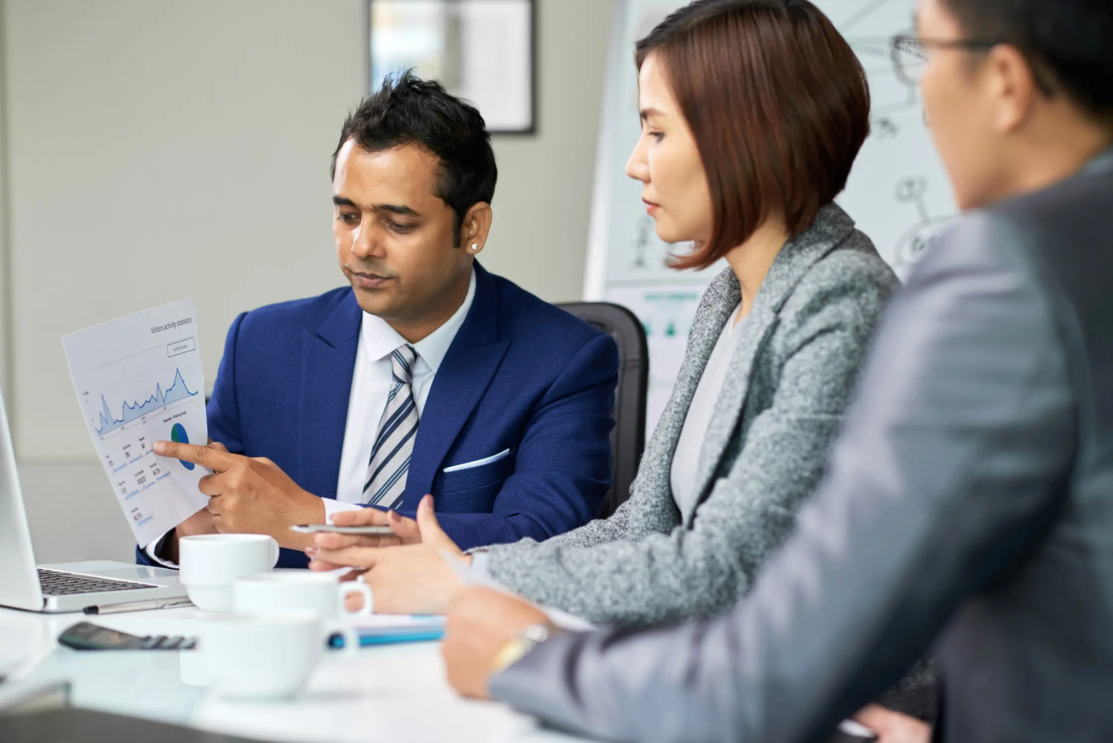 Investment manager presenting performance report to clients with printed charts in boardroom.
