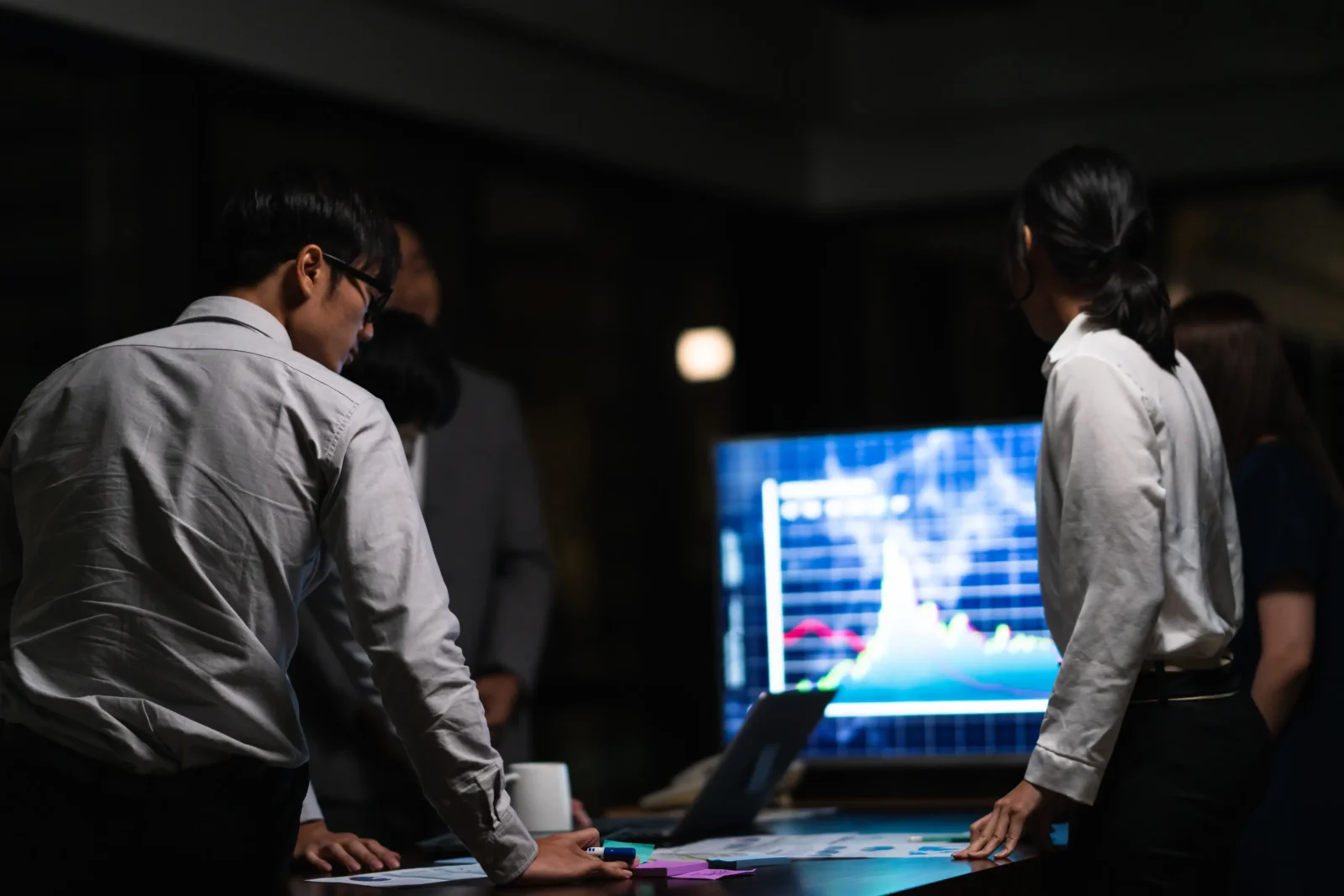 Investment team reviewing market volatility charts on large screen during evening strategy meeting.