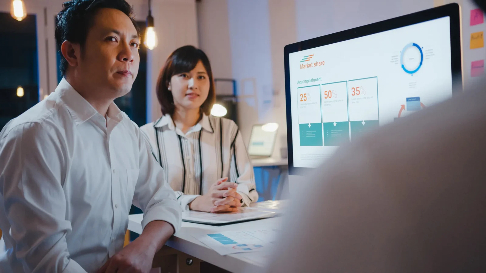 Investors listening to adviser presenting market share and performance metrics on screen in evening meeting.